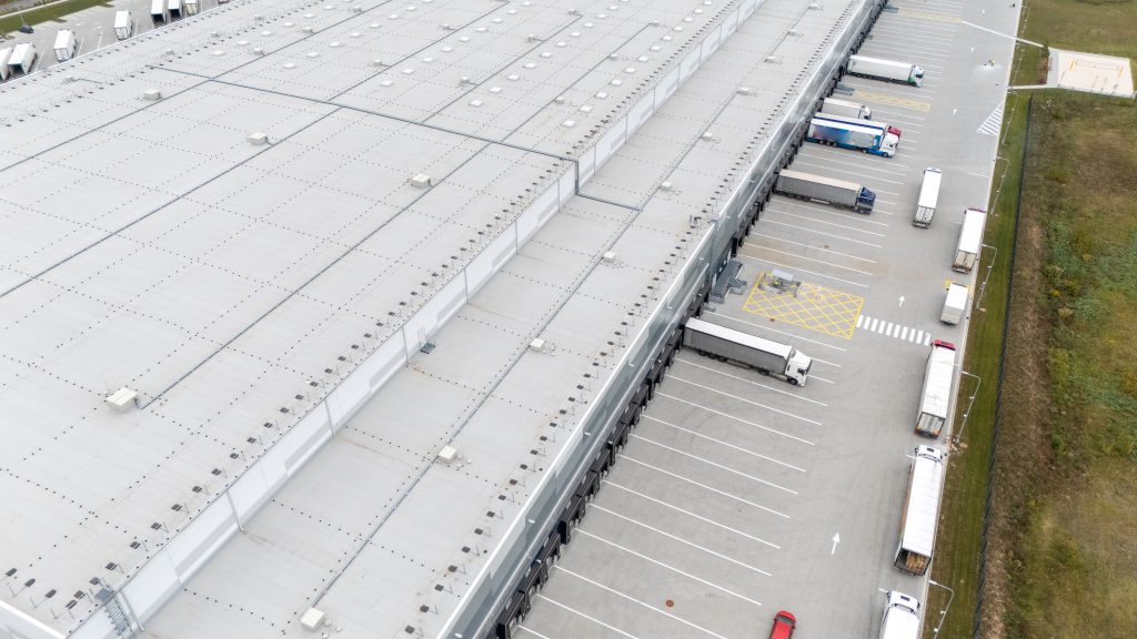 Aerial view of a large industrial warehouse with multiple loading docks and parked trucks and warehouse roof maintenance by JNG services